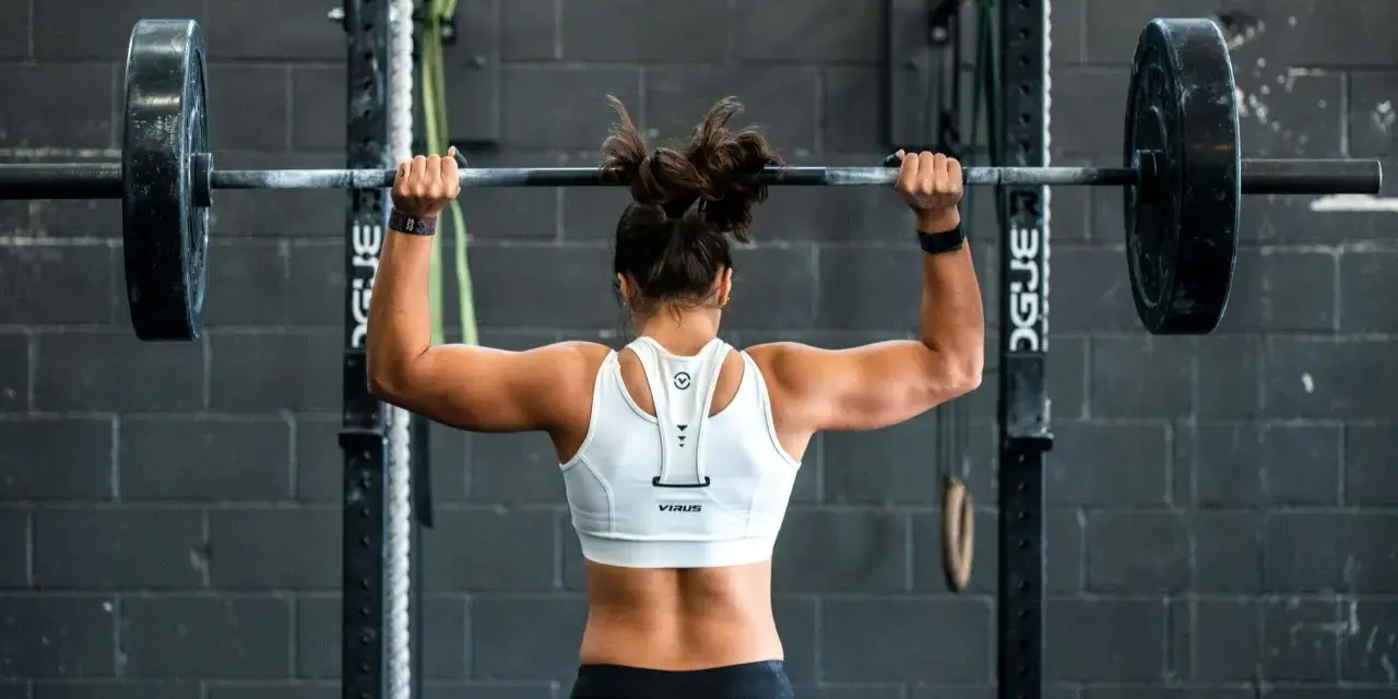 Femme musclée soulevant une barre chargée, prête pour un superset musculation intense.