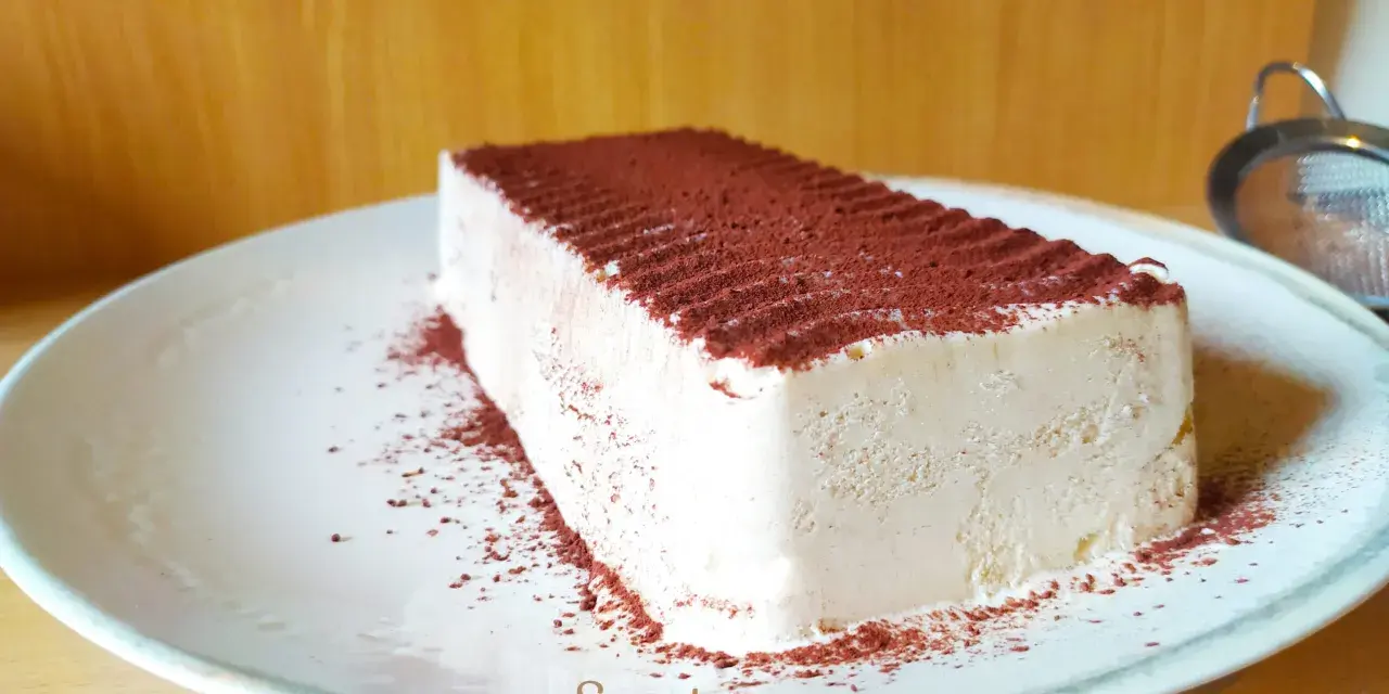 Un delizioso semifreddo al caffè, cosparso di cacao amaro, attende su un piatto bianco.