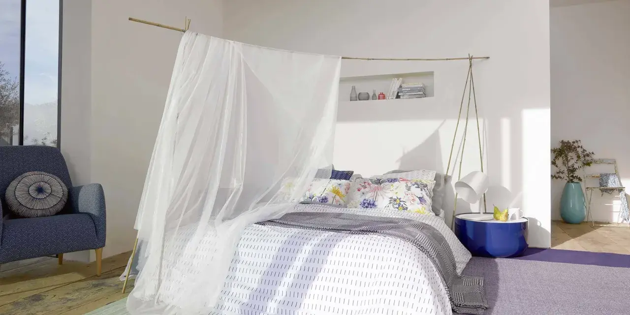 Acogedora habitación marinera con cama con dosel de tul, sillón azul y alfombras de colores.