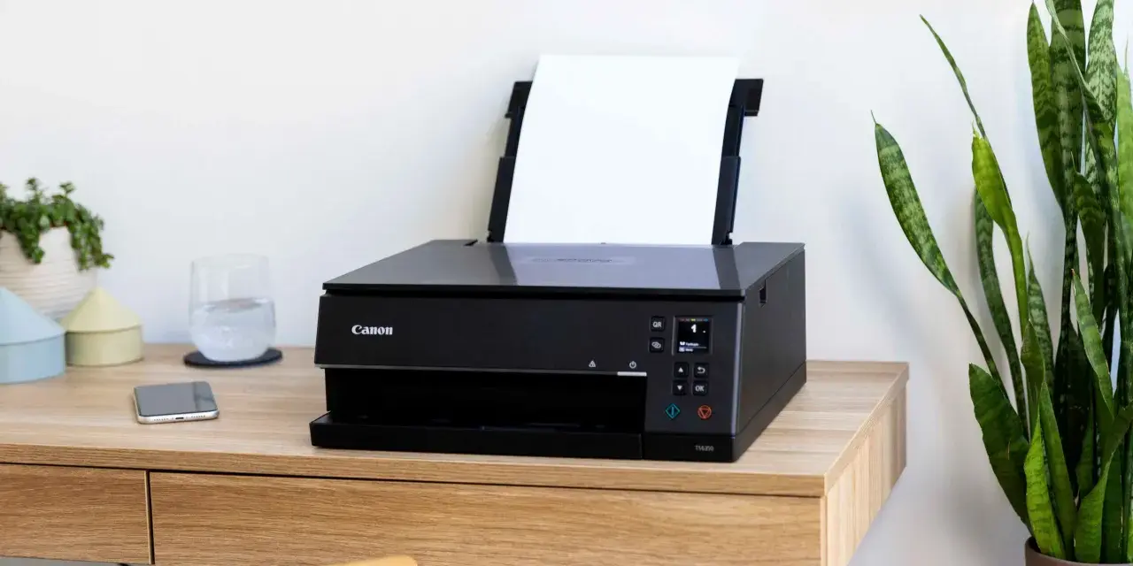 Schwarzer Canon Pixma Drucker mit WLAN verbinden. Ein Smartphone und ein Glas Wasser stehen daneben.
