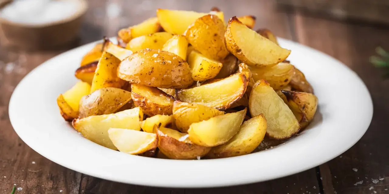 Patate al forno con buccia, dorate e croccanti, servite su un piatto bianco. Un contorno semplice e gustoso.