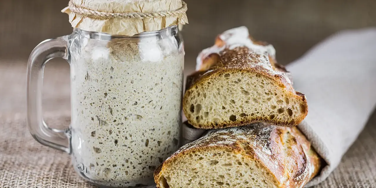 Ein Glas Sauerteig und zwei frisch gebackene Brotscheiben. So ist Sauerteig als Brot ein Genuss.