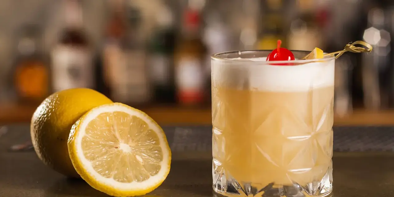 Orzeźwiający drink z amaretto, ozdobiony wiśnią i cytryną, stoi obok świeżych cytryn na barze.