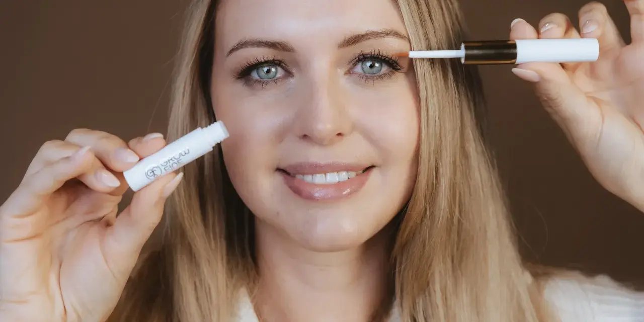 Frau mit blauen Augen trägt ein Serum auf ihre Wimpern auf, um sie wachsen zu lassen.