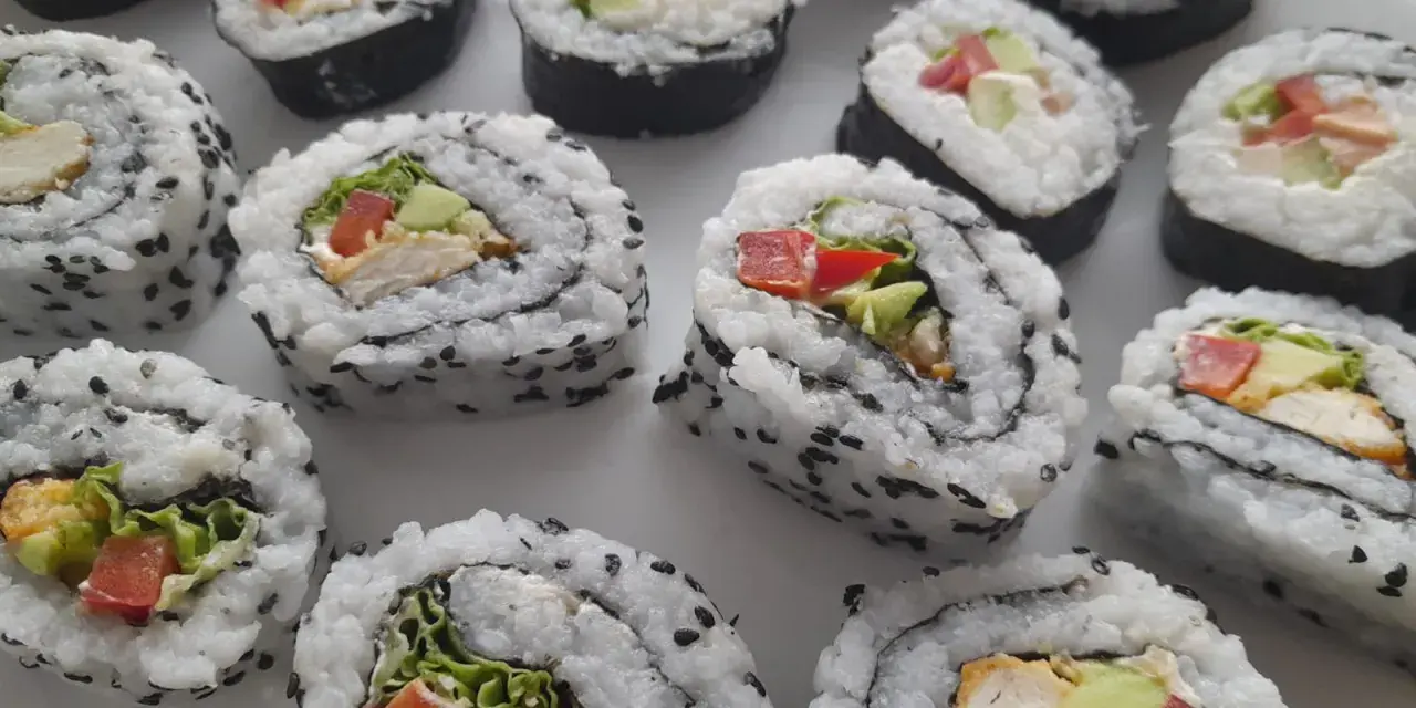 Pyszne domowe sushi z kurczakiem, awokado i warzywami, posypane czarnym sezamem.