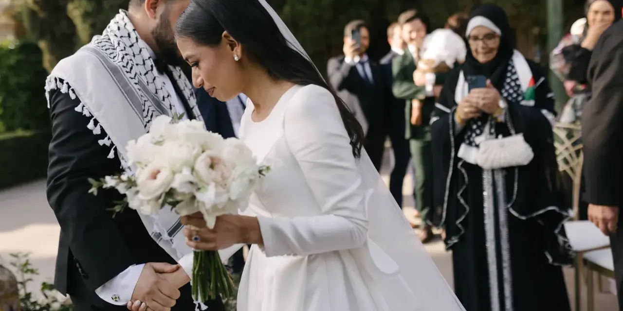 Panna młoda w białej sukni z welonem trzyma bukiet, pan młody w garniturze z szalem.