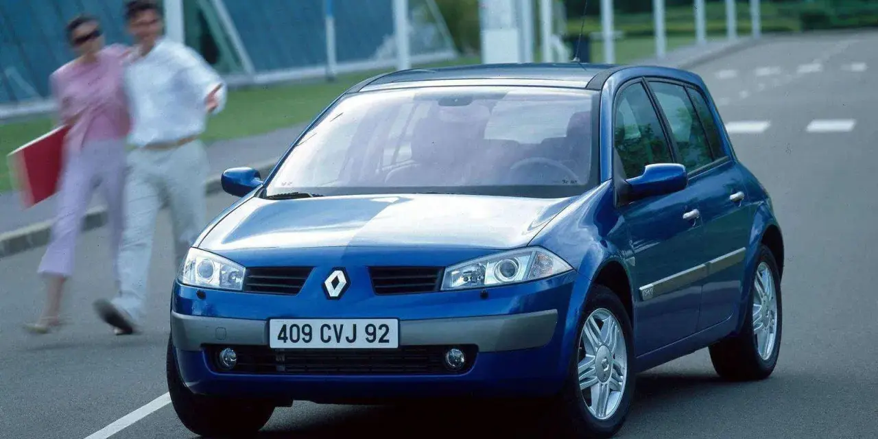 Niebieski Renault Megane 2 na drodze, z parą ludzi w tle.