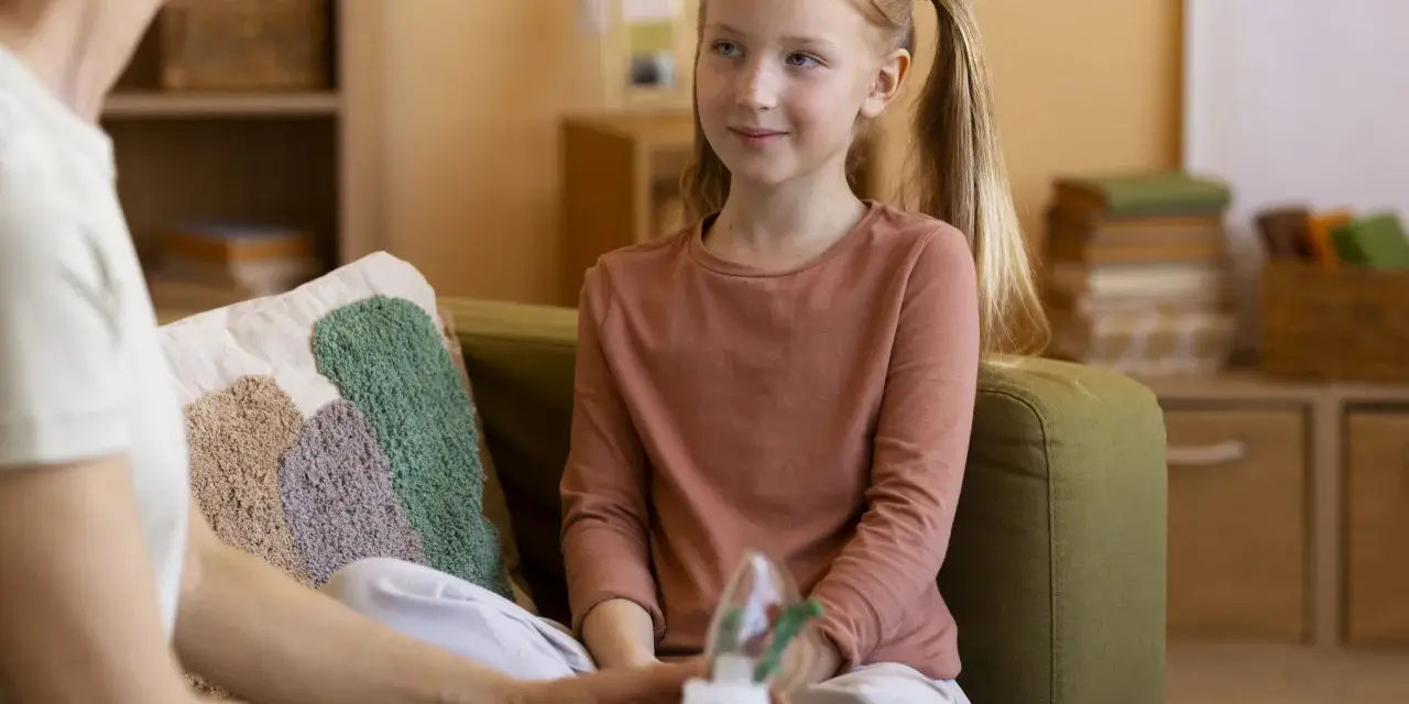 Rozmowa psychologa z rodzicem o zdrowiu dziecka. Dziewczynka z piegami słucha uważnie.