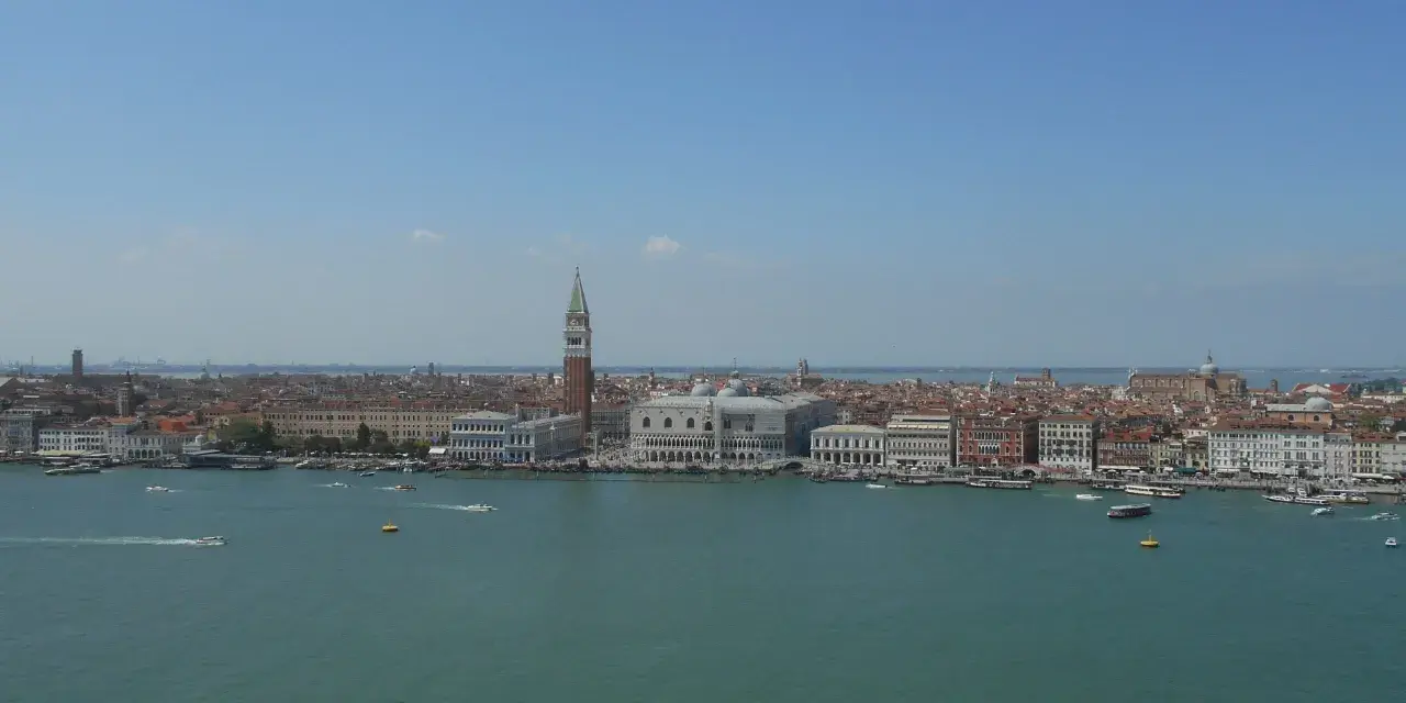 Venezia dall'alto, con il Campanile di San Marco che svetta tra i tetti rossi e il Canal Grande animato da vaporetti e barche.