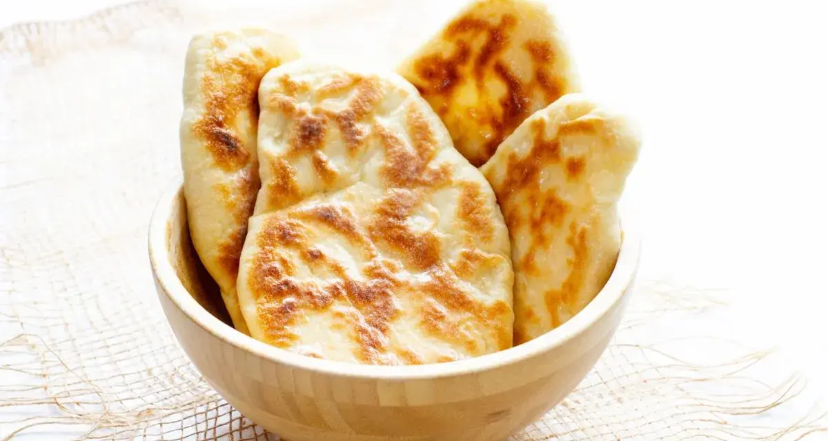 Kilka świeżo upieczonych chlebków naan w drewnianej misce.