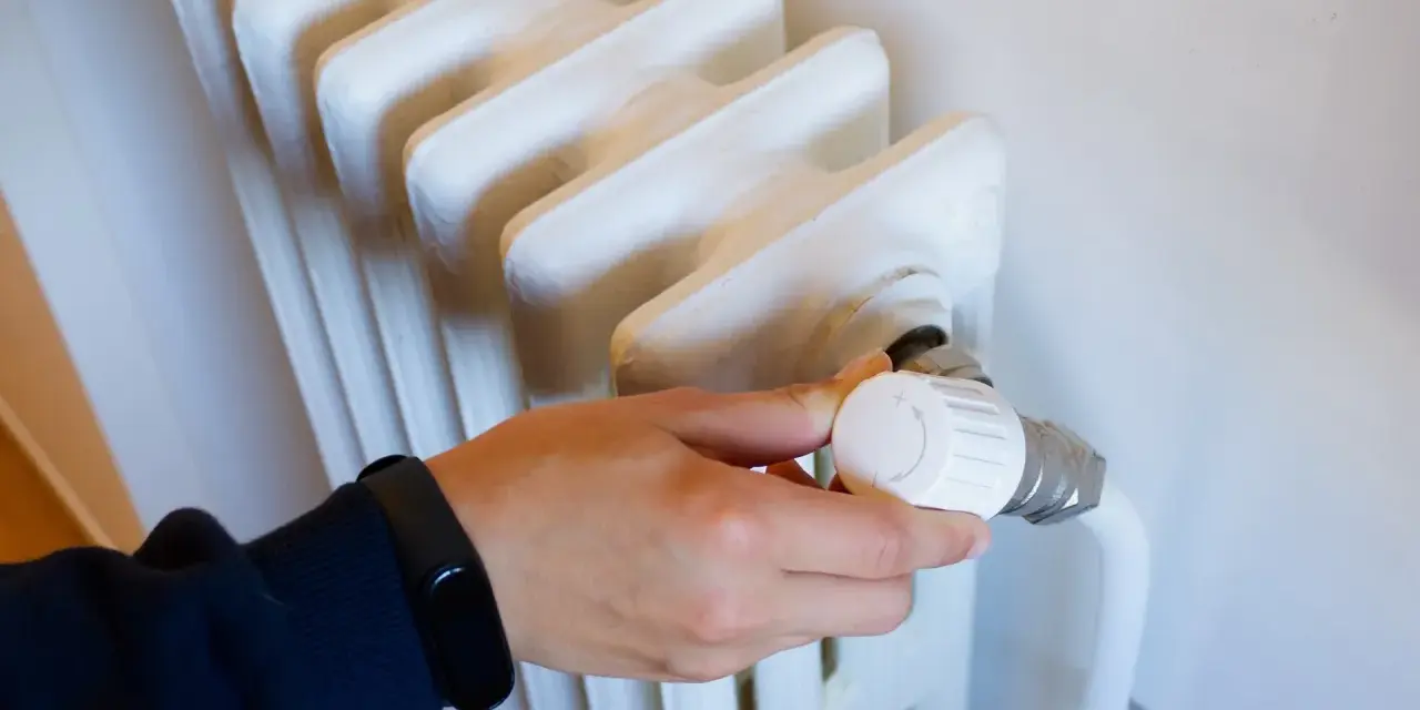 Ajustando el termostato de un radiador para optimizar la calefacción central en comunidades de vecinos.
