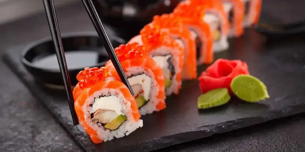 Chopsticks podnoszą kawałek sushi z łososiem i ikrą. Czy sushi jest lekkostrawne? Zależy od składników, ale ten wygląda apetycznie.