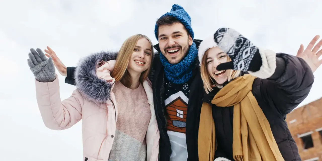 Drei Freunde genießen das Wandern im Winter. Sie tragen warme Kleidung wie Daunenjacken, Mützen und Handschuhe.