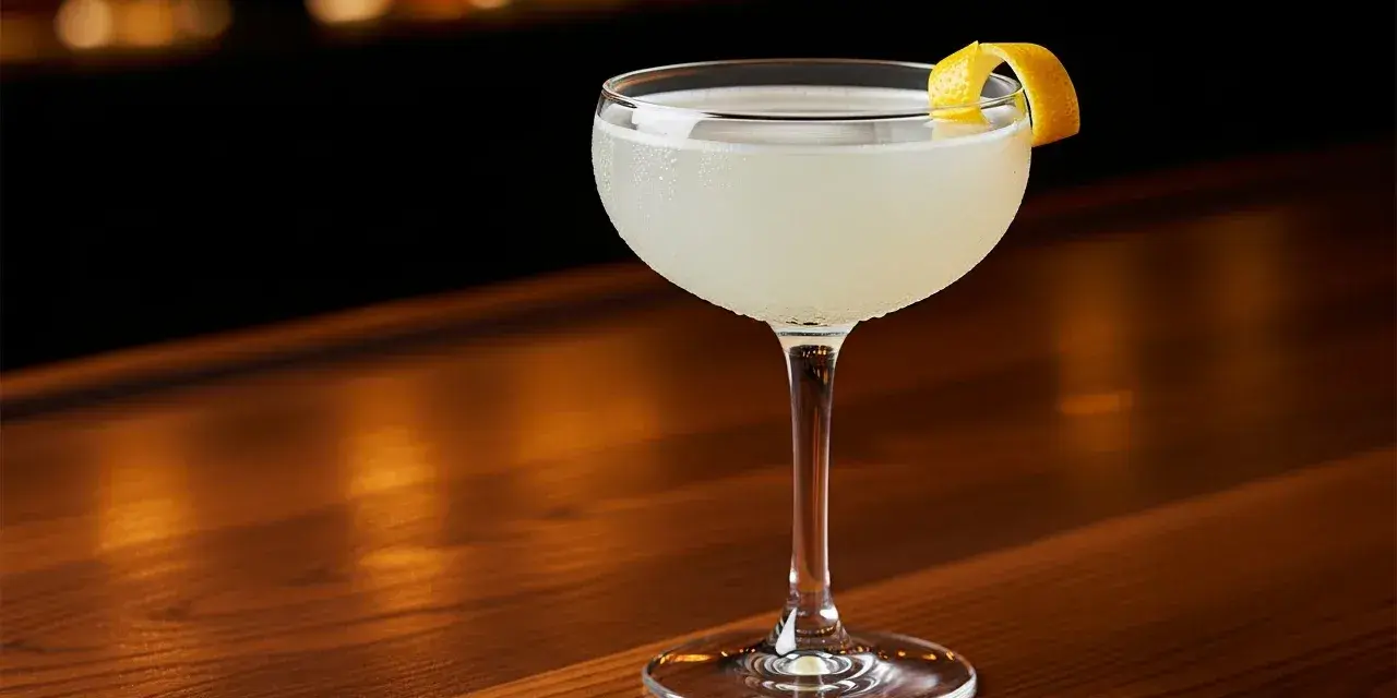 En elegant drink, en "white lady", står på en träbar. Den är garnerad med en citronskal.