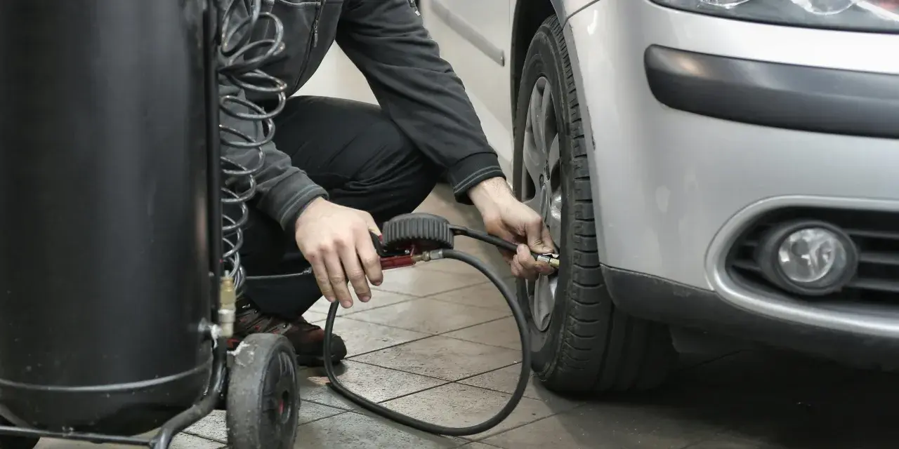 Un homme gonfle un pneu de voiture avec un manomètre et un compresseur.