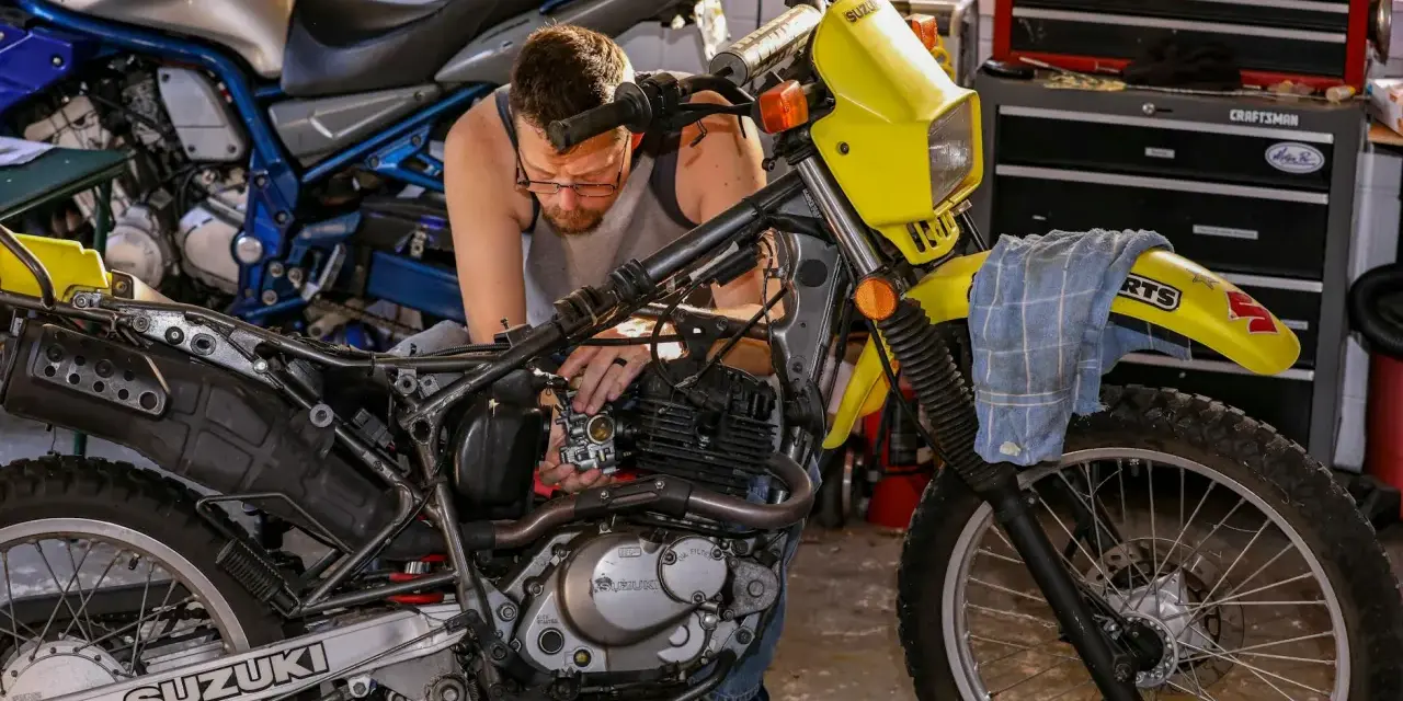Mężczyzna majstruje przy żółtym motocyklu Suzuki. Rozrusznik kręci, a motocykl nie odpala.