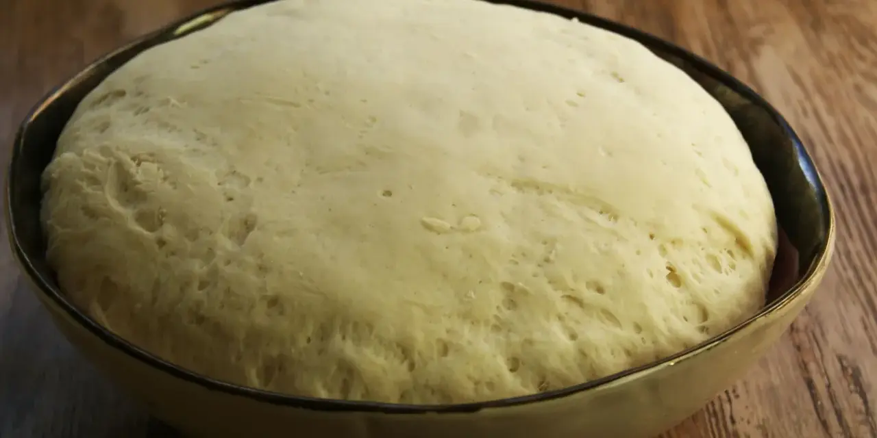 Wyrośnięte ciasto drożdżowe w misce, gotowe do pieczenia pizzy.