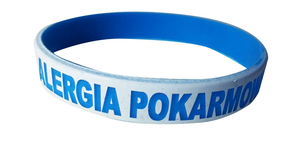 Niebieska opaska na ręce z napisem "ALERGIA POKARMOWA" informuje o problemach z jedzeniem.