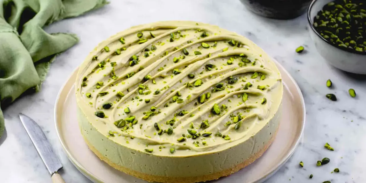 Cheesecake al pistacchio cremosa, decorata con granella verde brillante. Un dolce invitante pronto per essere gustato.