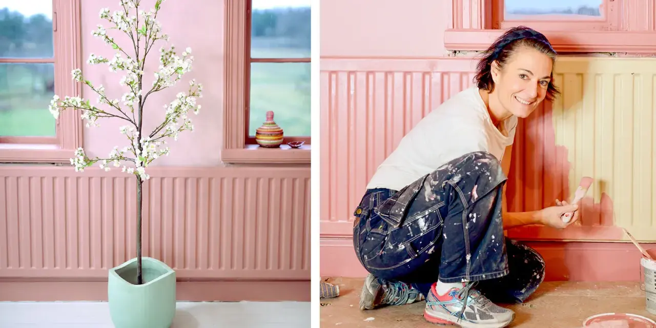 En kvinna målar en element rosa. Hon är klädd i blåa arbetsbyxor och en vit t-shirt. Bredvid henne står en konstgjord blommande körsbärsträd i en ljusgrön kruka.