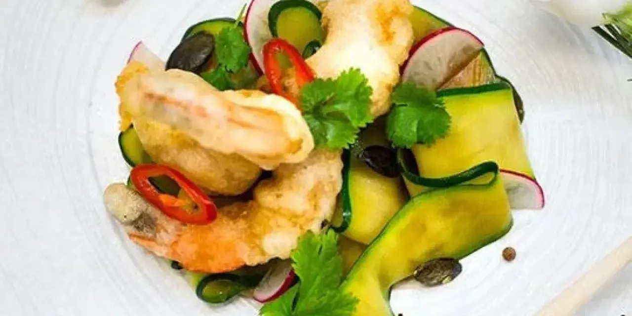 Chrupiące tempura do krewetek z cukinią, rzodkiewką i chili na białym talerzu.