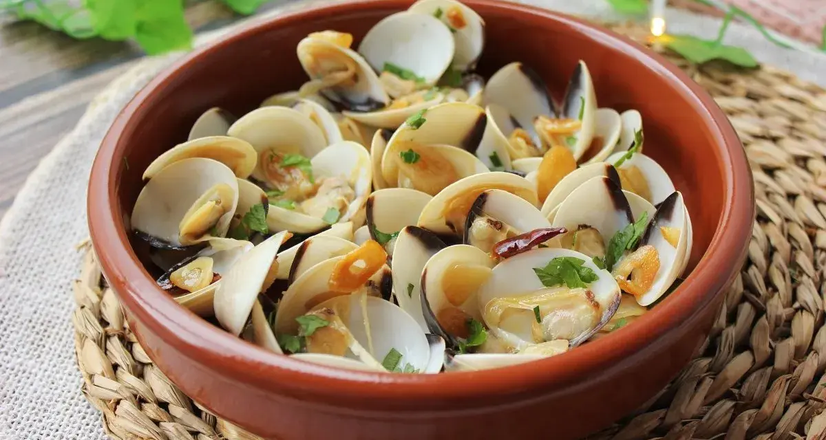 Deliciosas almejas al ajillo, servidas en una cazuela de barro, con ajo laminado y perejil fresco.