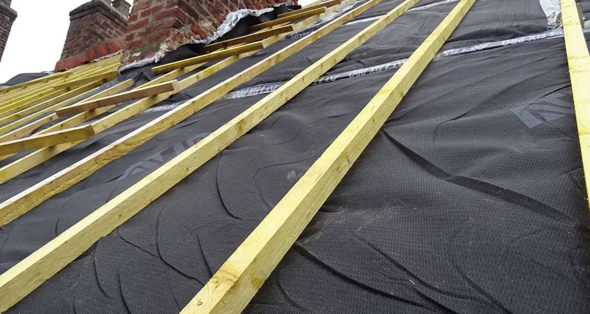 Charpente de toiture avec isolant noir et liteaux en bois, près de cheminées en brique.