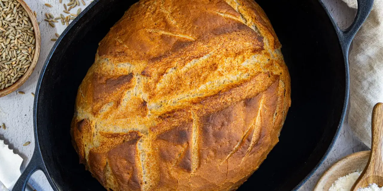 Ein goldbraunes Brot mit knuspriger Kruste liegt in einem Gusseisentopf. Dieses Brot kommt nicht aus dem Topf, sondern wurde darin gebacken.