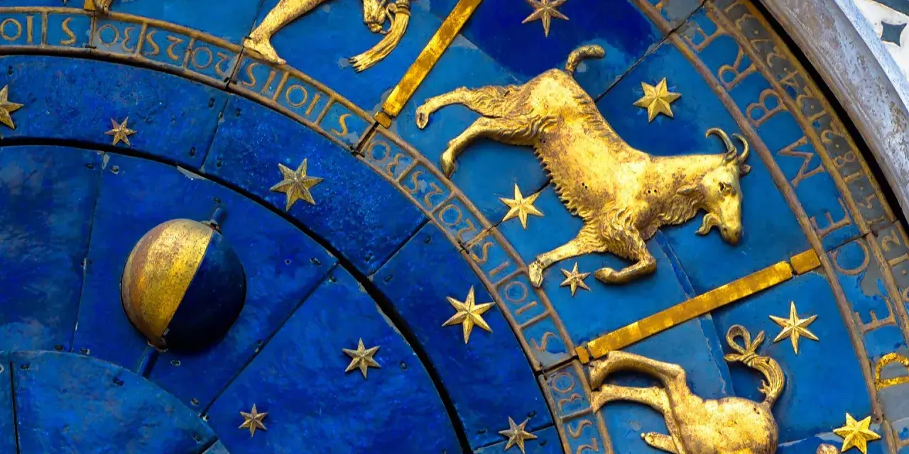 Złoty koziorożec na niebieskiej tarczy zegara astronomicznego, otoczony gwiazdami i cyframi. Dlaczego koziorożec milczy? Może czeka na swój czas.