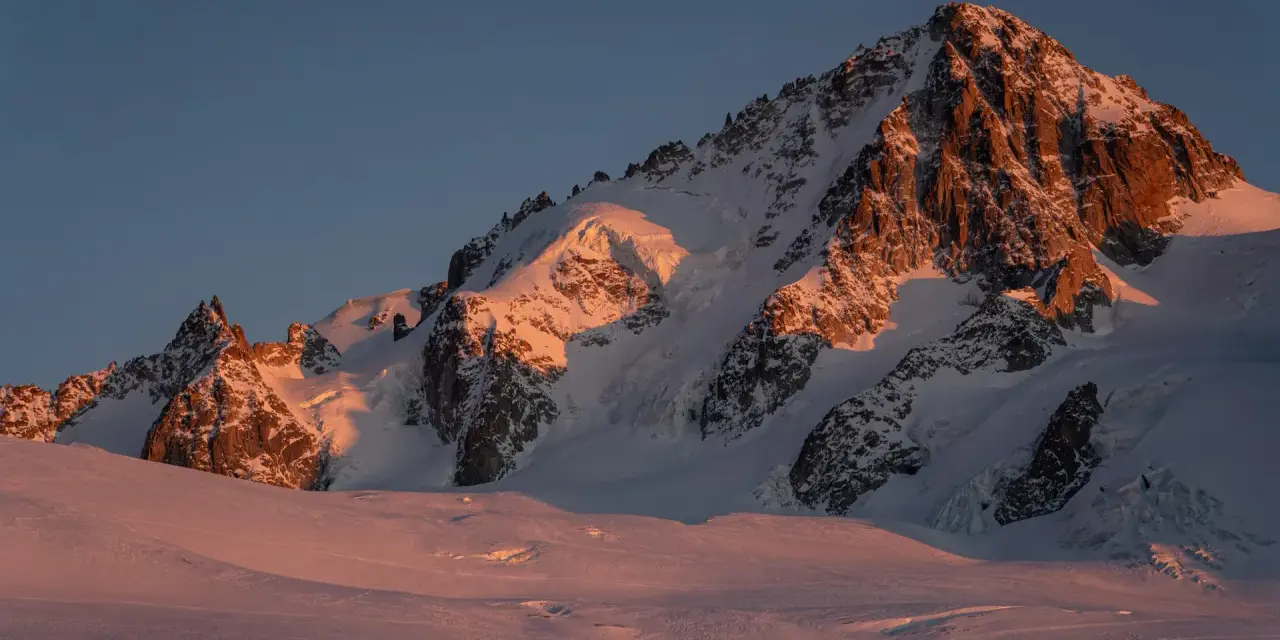 Ośnieżone szczyty Alp o wschodzie słońca, oświetlone złotym blaskiem. Widok na trasę Haute Route, gdzie lodowce i skaliste zbocza tworzą majestatyczny krajobraz.