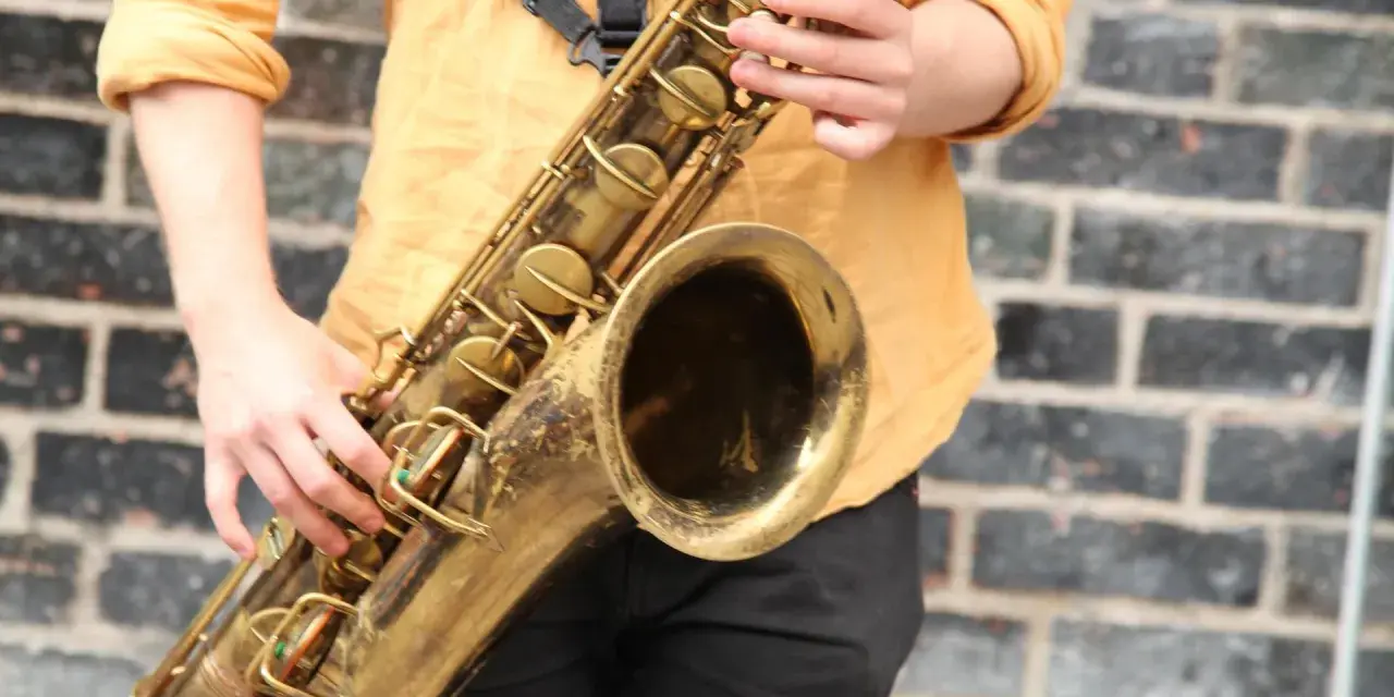 Hände spielen ein goldenes Saxophon. Obwohl es aus Metall ist, ist das Saxophon ein Holzblasinstrument, da der Ton durch ein Rohrblatt erzeugt wird.