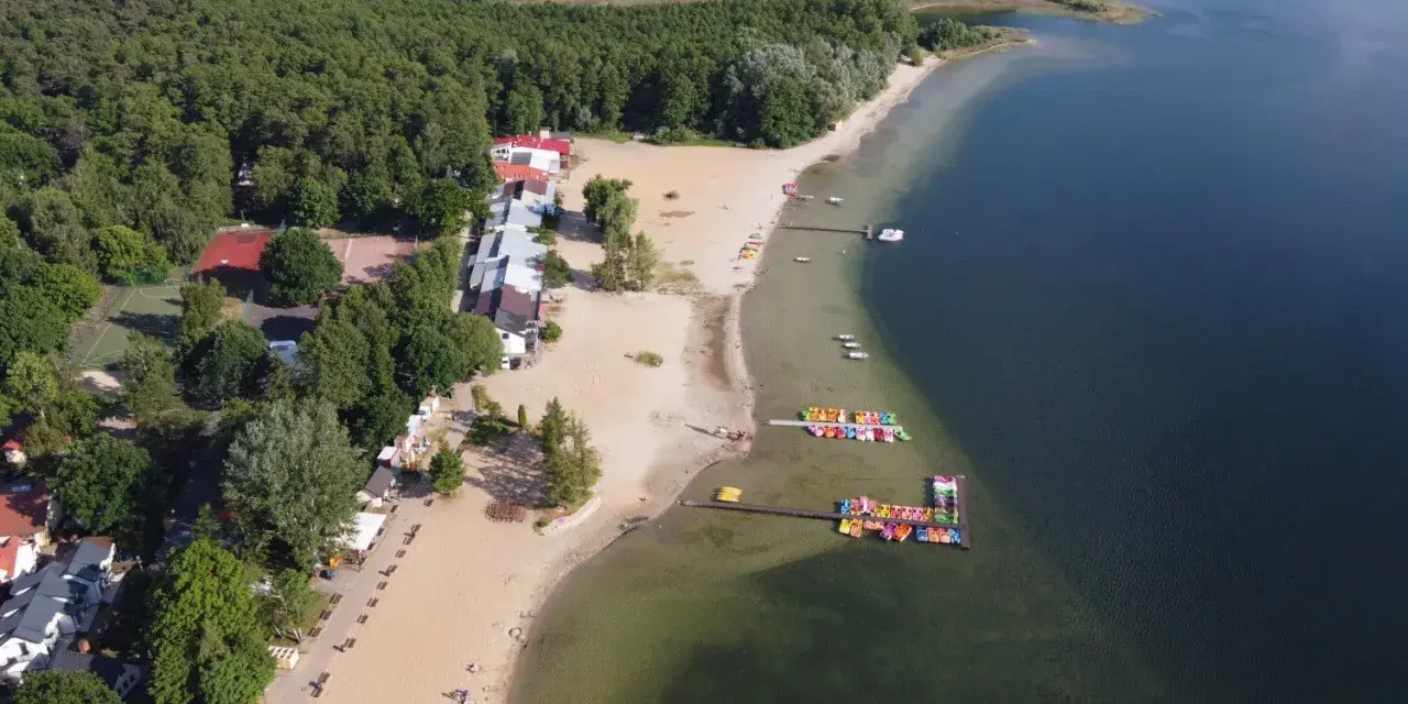 Skorzęcin jezioro z lotu ptaka: piaszczysta plaża, kolorowe rowery wodne, budynki i las.