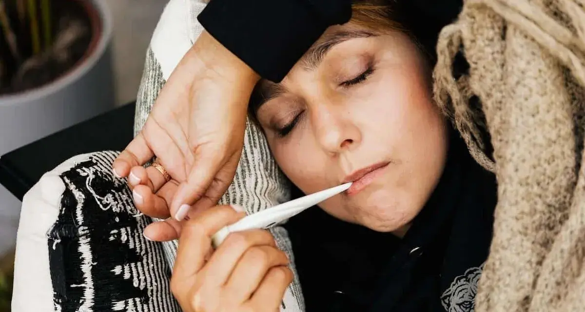 Kobieta z gorączką mierzy temperaturę. To ważny element przy ustalaniu podstawy wymiaru zasiłku chorobowego.