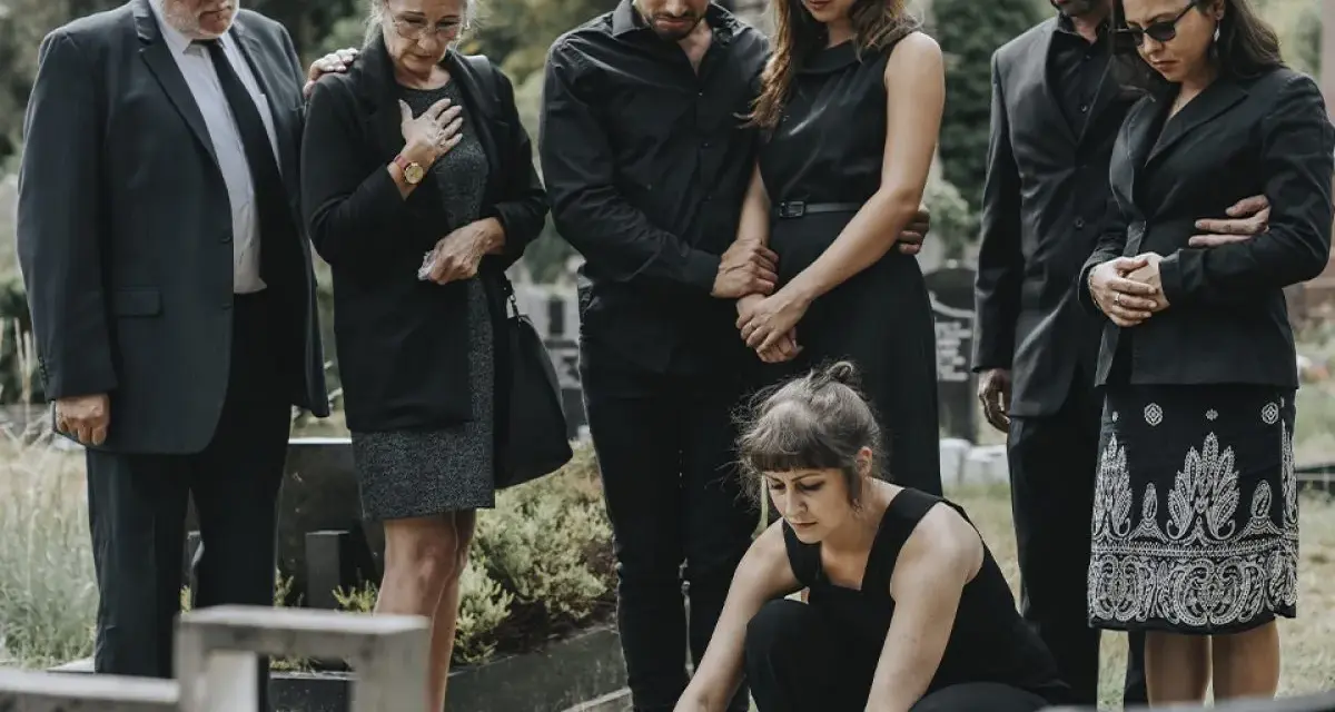 Famiglia in lutto, vestiti di nero, si riunisce al cimitero. Un esempio di come vestirsi a un funerale, con abiti sobri e rispettosi.
