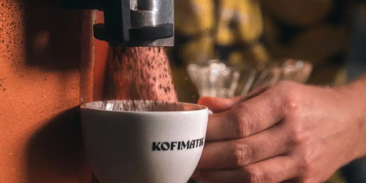 Mielona kawa spada do filiżanki z napisem "Kofimatik". Idealna baza do kawy z likierem kawowym Baileys.