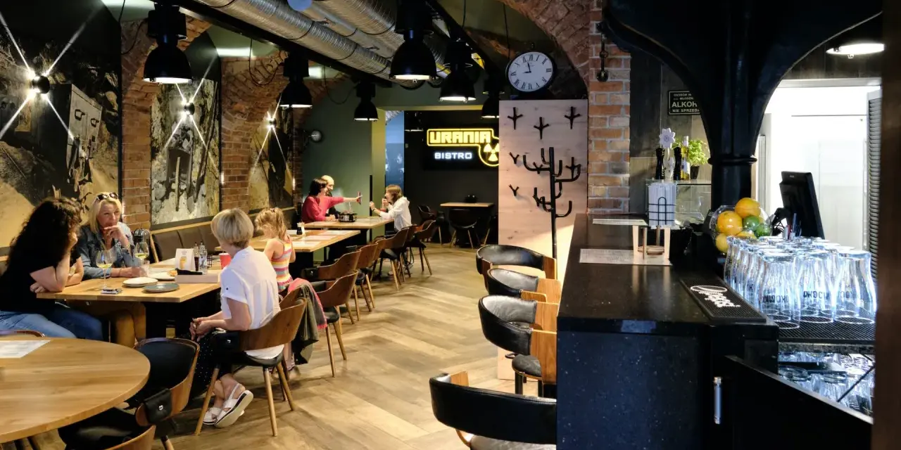 Wnętrze restauracji Urania Bistro z ludźmi przy stołach i barem.