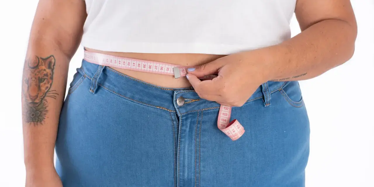 Persona plus size se mide la cintura con una cinta métrica rosa.