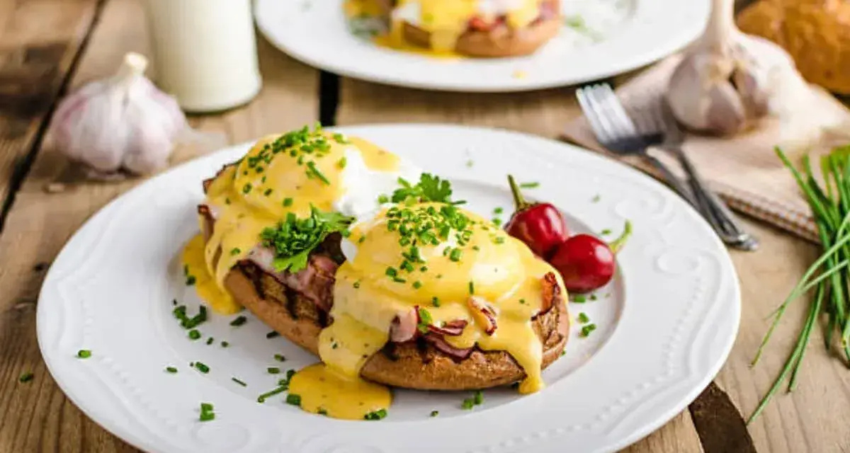 Huevos Benedictinos en plato blanco con salsa holandesa, perejil y chiles rojos.