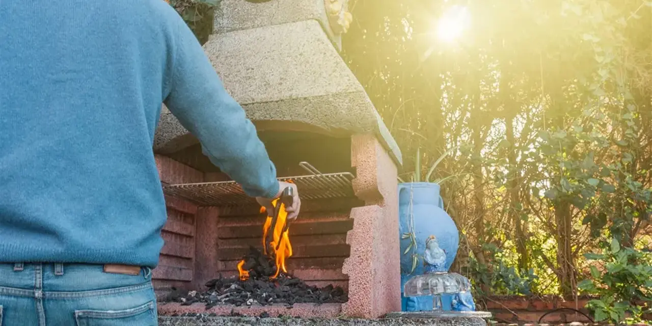 Hombre aviva las brasas en una de las **tipos de barbacoas de obra**, lista para una parrillada.