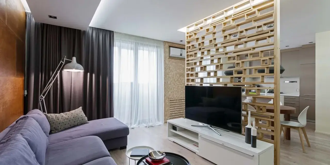 Acogedor salón de 18 metros cuadrados con sofá morado, lámpara de pie y separador de ambiente de madera.