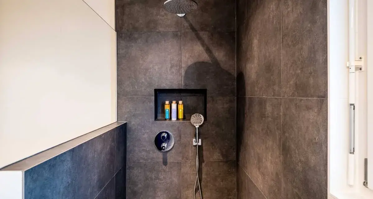 Ducha moderna con tabique de obra y muro de cristal. Incluye alcachofa de lluvia, grifería empotrada y nicho con botes de champú.