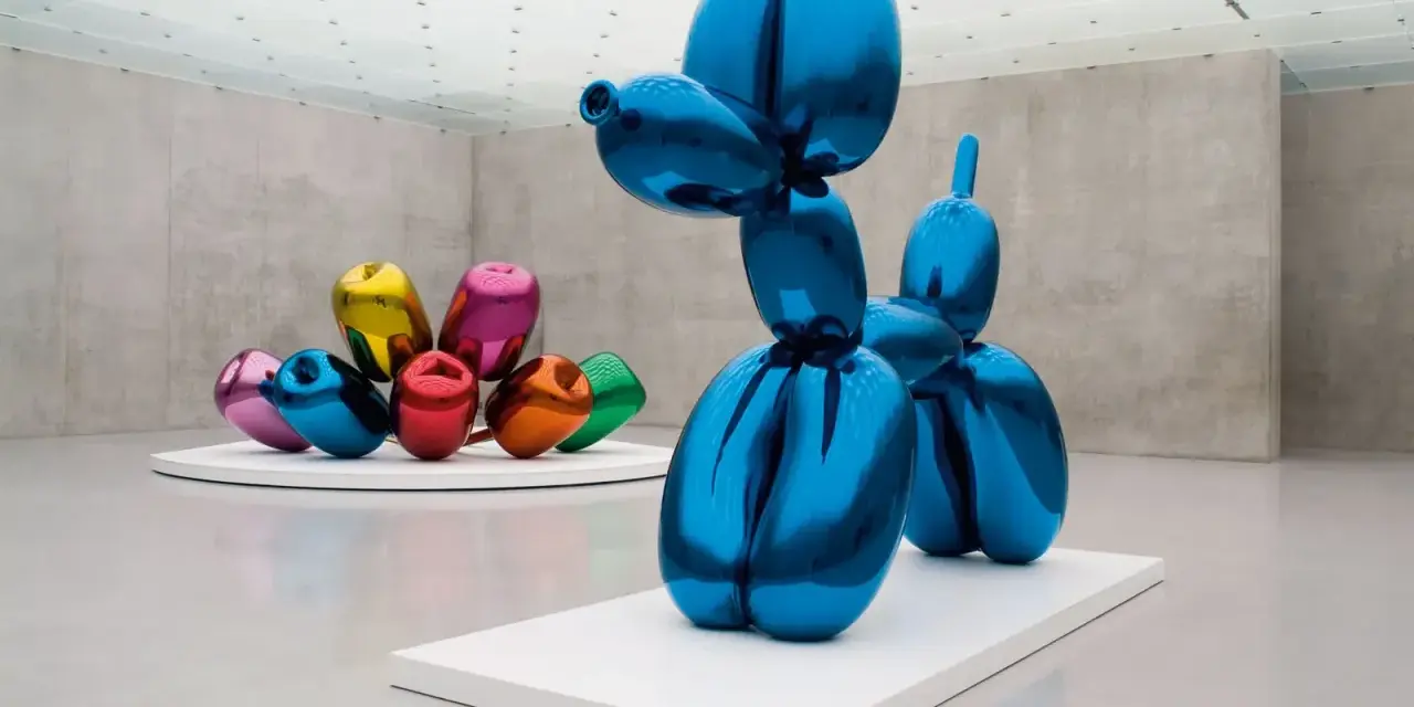 Un chien ballon bleu iconique de Jeff Koons, reflétant l'espace d'exposition. D'autres sculptures de ballons colorés sont visibles en arrière-plan.