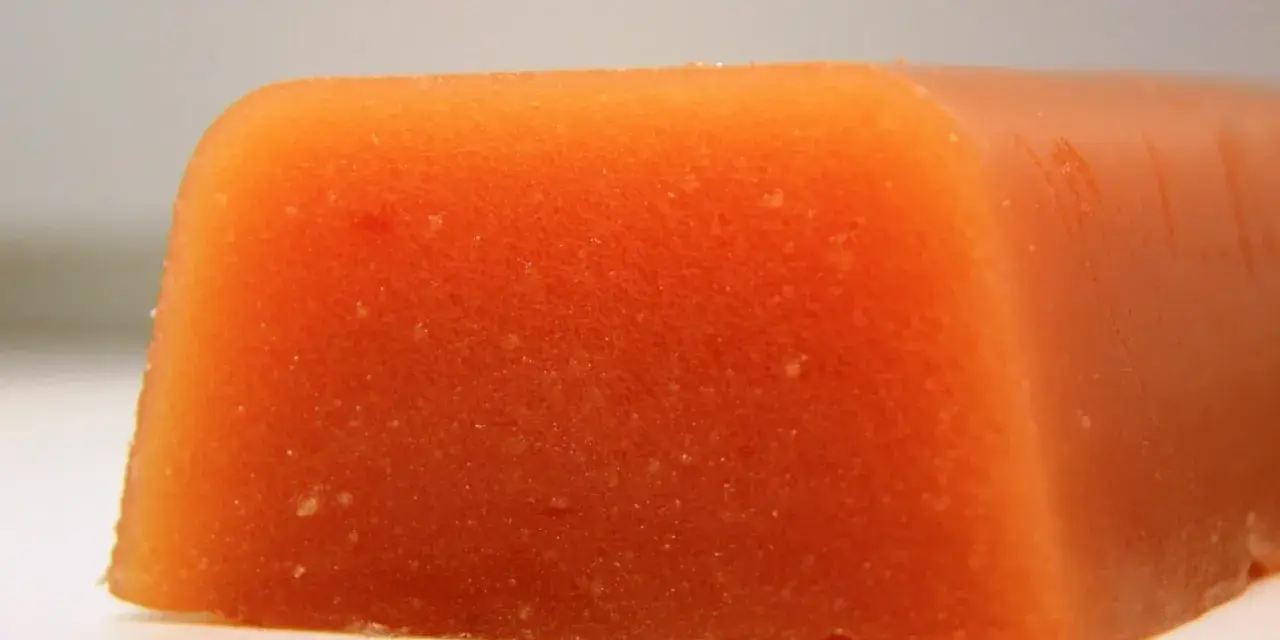 Bloque naranja de carne de membrillo, con textura granulada y bordes redondeados.