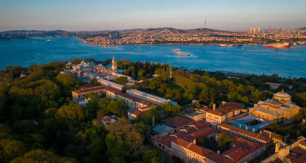 Aerial view of the Topkapi Palast complex, nestled amongst lush greenery, with the Bosphorus Strait and Istanbul skyline in the background.