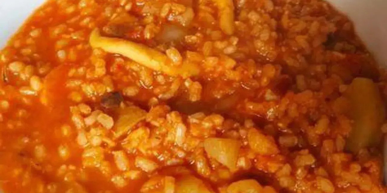 Arroz caldoso con trozos de marisco y verduras en salsa rojiza.