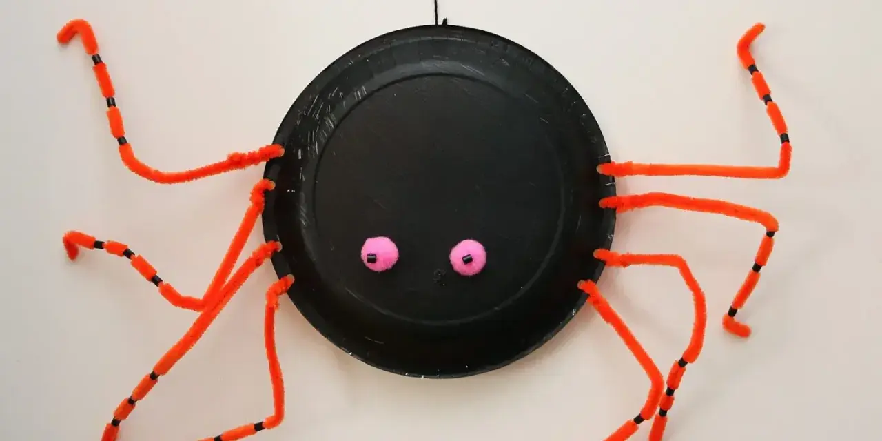 En svart spindel av piprensare med rosa ögon hänger från en tråd.