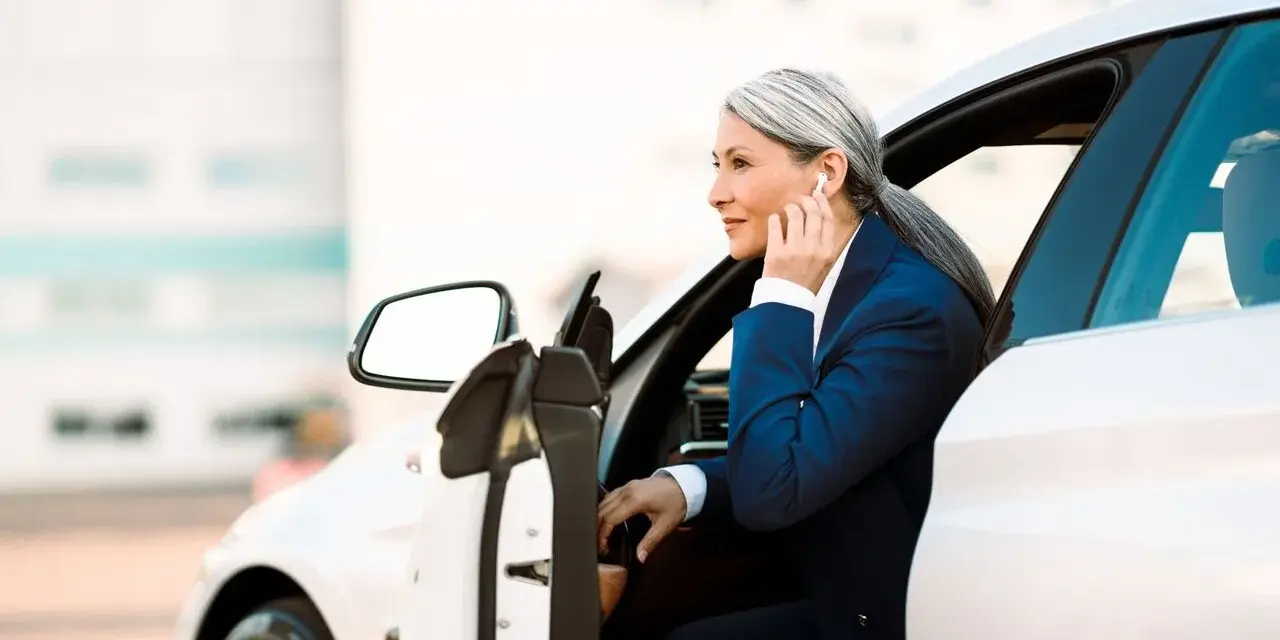 Elegancka kobieta w garniturze wsiada do białego auta. To jej auto na abonament, idealne do biznesowych podróży.