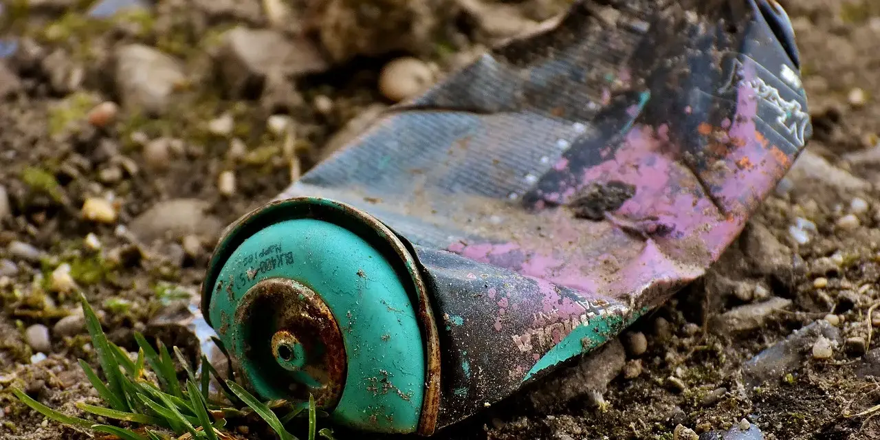 Lata de aerosol aplastada y oxidada en el suelo, un ejemplo de las causas de la contaminación.