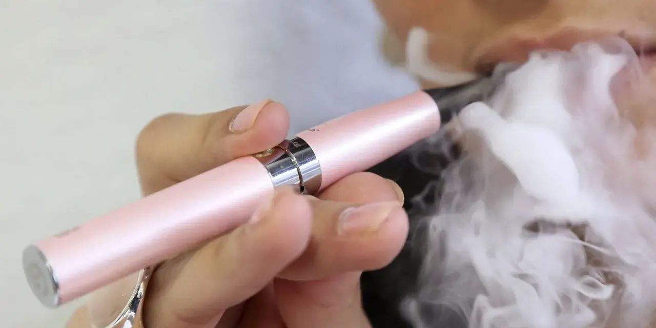 Persona exhala vapor de un cigarrillo electrónico rosa. ¿Qué es peor el vaper o el tabaco?