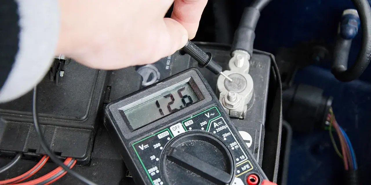 Sprawdzanie prawidłowego napięcia akumulatora multimetrem. Wynik 12.6V wskazuje na dobry stan.